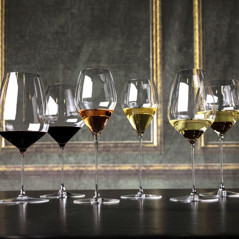 Eine Reihe von sechs Weingläsern, jedes mit unterschiedlichen Weinsorten gefüllt, steht auf einer schwarzen Tischplatte. Der Hintergrund zeigt eine elegante strukturierte Wand mit dezenten vertikalen und horizontalen Goldverzierungen.