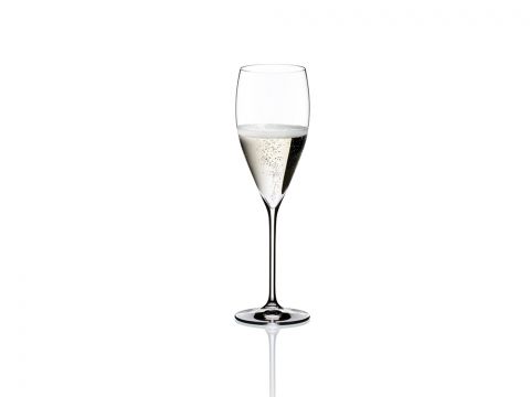 Ein gefülltes Champagnerglas steht vor einem schlichten weißen Hintergrund. In der hellen Flüssigkeit steigen Blasen auf, was dem Glas ein elegantes und festliches Aussehen verleiht. Das Glas ist hoch und schlank und zeigt den funkelnden Inhalt.
