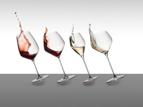 Vier Weingläser mit Flüssigkeitsspritzern: zwei mit Rotwein, eines mit Weißwein und eines fast leer. Der Hintergrund ist ein neutraler Farbverlauf.
