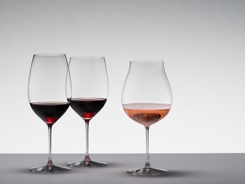 Drei Weingläser stehen auf einer glatten Fläche vor hellgrauem Hintergrund. Zwei davon enthalten Rotwein und stehen nebeneinander, während das dritte, mit einem Rosé-Schaumwein gefüllt, etwas abseits auf der rechten Seite steht.