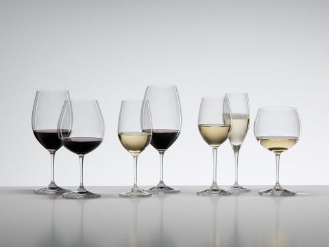 Eine Vielzahl von Weingläsern, jedes mit unterschiedlichen Weinsorten gefüllt, sind in einer Reihe auf einer reflektierenden Oberfläche angeordnet. Die Sammlung umfasst Rot- und Weißweine sowie Champagner vor einem einfachen weißen Hintergrund.
