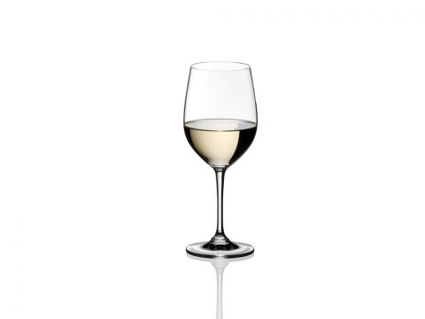 Ein klares, mit Weißwein gefülltes Weinglas steht zentriert vor einem schlichten weißen Hintergrund, darunter ist eine reflektierende Oberfläche zu sehen.