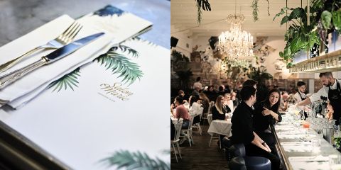 Ein elegantes Restaurant-Interieur mit einem Kronleuchter, Hängepflanzen und Gästen, die an einer Bar sitzen. Eine Nahaufnahme eines gedeckten Tisches zeigt eine Speisekarte mit der Aufschrift „Salon Marie“.
