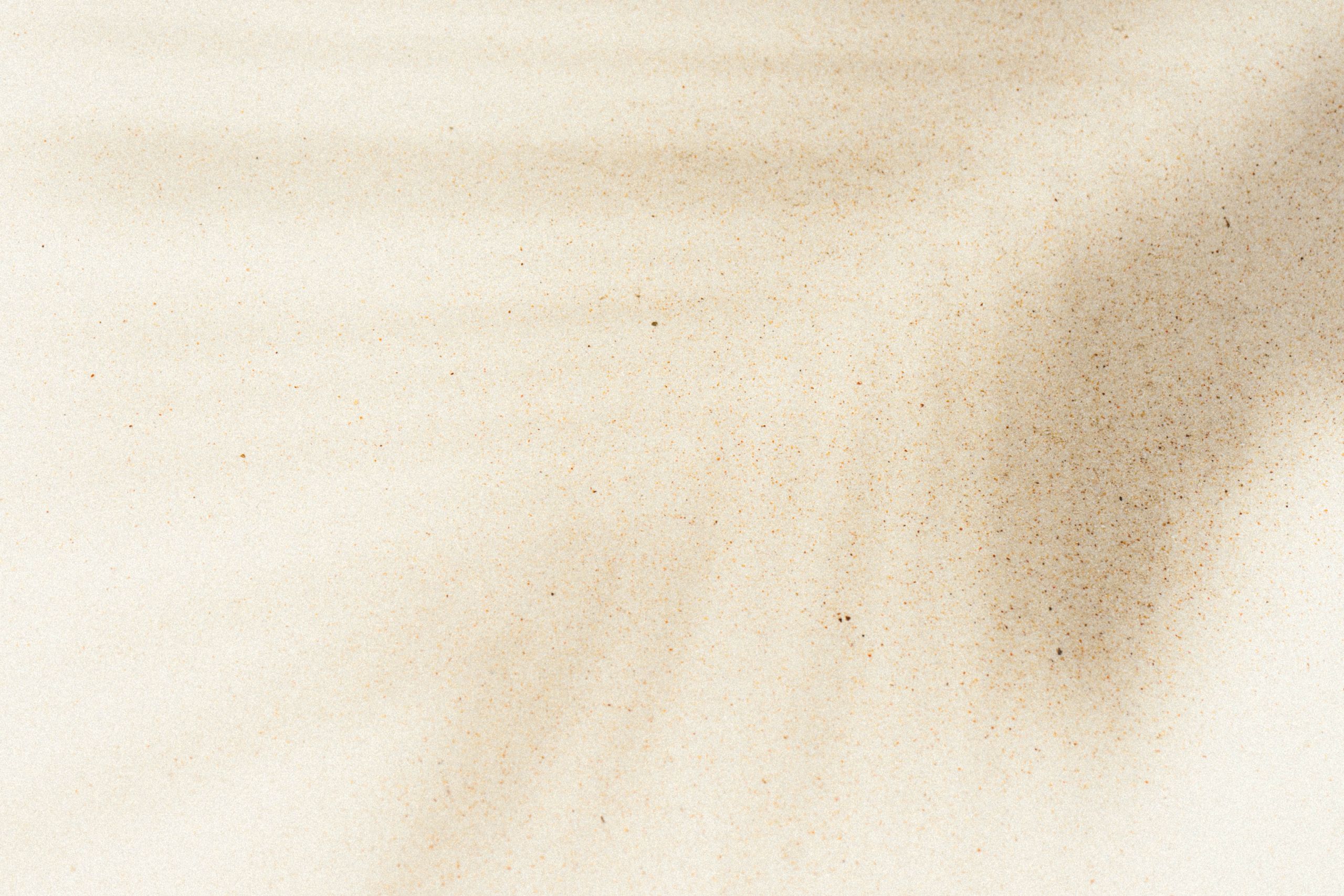 Eine Nahaufnahme von feinem, hellbeigem Sand mit subtilen Schatten und Texturen, die ein zartes Muster auf der Oberfläche erzeugen.