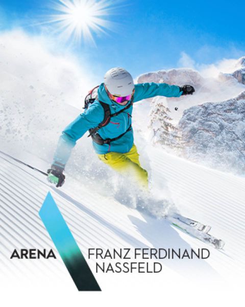 Ein Skifahrer in einer leuchtend türkisen Jacke und gelben Hosen fährt einen schneebedeckten Hang hinunter. Die Sonne scheint hell am klaren blauen Himmel und wirft Schatten auf den Pulverschnee. Der Text lautet „Arena Franz Ferdinand Nassfeld“.