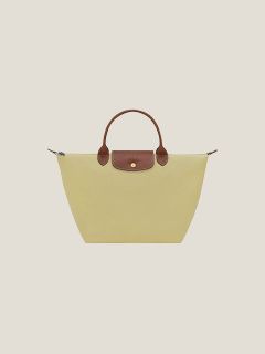 Gelbe Tragetasche mit braunen Ledergriffen und Klappe, die vor einem einfarbig beigen Hintergrund präsentiert wird.