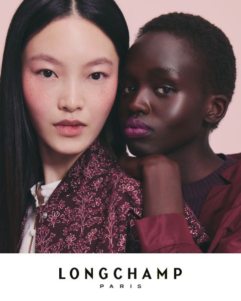 Zwei Frauen stehen dicht beieinander vor einem rosa Hintergrund und präsentieren eine Kollektion von Longchamp Paris. Eine trägt eine gemusterte Jacke, die andere ein einfarbiges Oberteil, beide sind natürlich geschminkt und haben leicht geöffnete Lippen. Darunter wird der Text von Longchamp Paris angezeigt.