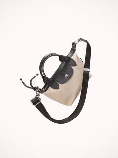 Auf weißem Hintergrund ist eine stilvolle Handtasche mit beigem Korpus und schwarzer Lederklappe abgebildet. Sie hat einen schwarzen Riemen mit silberner Schnalle und einen Kordelzugverschluss.