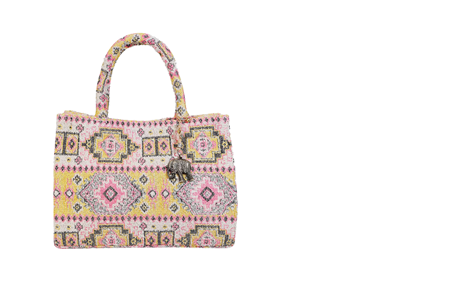 Eine farbenfrohe Einkaufstasche mit einem geometrischen Muster in Rosa, Gelb und Schwarz. Sie hat zwei Griffe und an einem davon hängt ein Anhänger in Elefantenform. Der Hintergrund ist weiß.