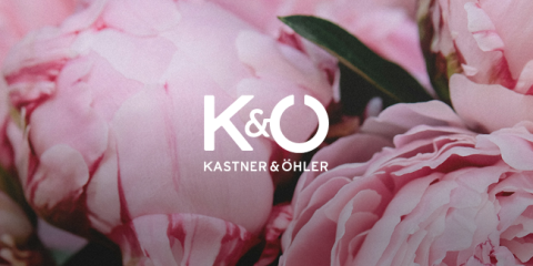 Nahaufnahme zartrosa Pfingstrosen mit dem Logo „K&Ö“ und dem Text „Kastner & Öhler“ in Weiß darüber. Die umgebenden Blütenblätter bilden einen üppigen, blumigen Hintergrund.