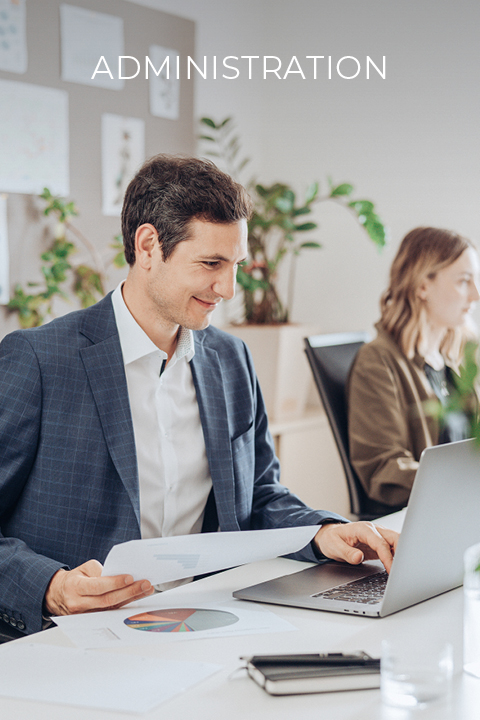 Ein Mann im Anzug arbeitet an einem Schreibtisch mit einem Laptop und hält Papiere in der Hand. Im Hintergrund sitzt eine Frau und arbeitet ebenfalls. Oben steht das Wort „Verwaltung“. Im Büro sind Pflanzen und Diagramme zu sehen.