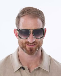 Ein Mann mit kurzen Haaren und Bart trägt eine große, quadratische Sonnenbrille mit dunklen Gläsern. Er trägt ein beiges Hemd mit Kragen und lächelt. Der Hintergrund ist schlicht weiß.