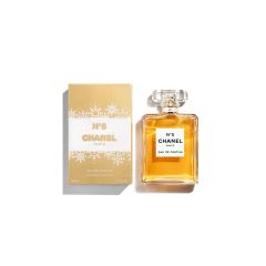 Eine Flasche Chanel No. 5 Eau de Parfum ist neben der gold-weißen Verpackung abgebildet. Die Flasche ist rechteckig, hat einen durchsichtigen Verschluss und enthält bernsteinfarbenes Parfüm. Die Verpackung ist elegant und ikonisch.