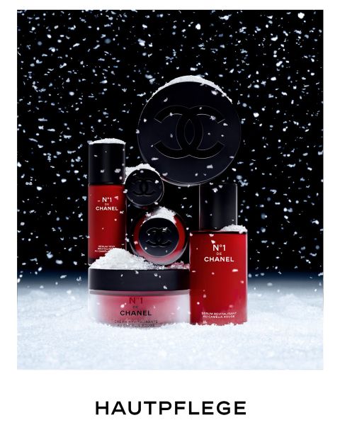 Auf Schnee vor dunklem Hintergrund sind Hautpflegeprodukte von Chanel mit rot-schwarzer Verpackung zu sehen. Um sie herum fallen Schneeflocken. Unten steht das Wort „HAUTPFLEGE“.