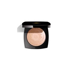 Ein schwarzes Kompaktetui mit einem beigefarbenen gepressten Puder darin, auf dessen Oberfläche ein aufwendiges Sonnenstrahlen-Design geprägt ist. Das Kompaktetui ist geöffnet und zeigt das Puder. Auf dem Deckel befindet sich ein Logo. Der Hintergrund ist weiß.
