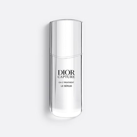 Eine schlanke, durchscheinende Flasche Dior Capture OX-C Treatment Le Sérum. Die Flasche ist hoch und geschwungen, hat ein minimalistisches Design und einen schwarzen Text auf der Vorderseite. Auf einem hellgrauen Hintergrund.