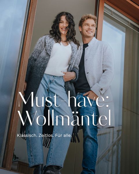 Eine lächelnde Frau und ein lächelnder Mann stehen draußen zusammen, beide tragen elegante graue Wollmäntel und blaue Jeans. Der Text auf dem Bild lautet: "Must-have: Wollmäntel. Klassisch. Zeitlos. Für alle.