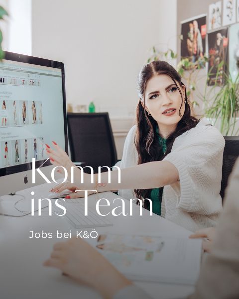Eine Frau mit langen dunklen Haaren und weißem Pullover zeigt auf einen Computerbildschirm, auf dem Kleidungsstücke angezeigt werden. Sie scheint etwas mit einer anderen Person zu besprechen. Der Text lautet „Komm ins Team“ und „Jobs bei K&O“.