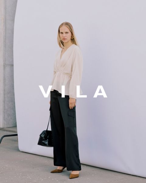 Fünf Frauen in Freizeitkleidung, darunter Jeans und Oberteile in neutralen Farben, stehen eng beieinander und lächeln vor einem schlichten Hintergrund. Der überlagerte Text lautet "Vila Clothes".