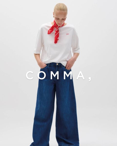 Eine Frau in einem karierten Mantel und goldenen Accessoires posiert mit einem hellbraunen und weißen Hund in einem passenden karierten Outfit. Das Wort "COMMA" erscheint in großer weißer Schrift quer über das Bild.