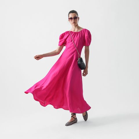 Eine Person trägt ein passendes gemustertes Kurzarmhemd und Shorts, schwarze spitze Schuhe, eine Sonnenbrille und eine kleine schwarze Handtasche und geht selbstbewusst vor einem schlichten weißen Hintergrund.