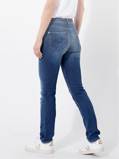 Eine Person, die ein weißes T-Shirt, blaue Slim-Fit-Jeans und weiße Turnschuhe trägt, steht vor einem schlichten weißen Hintergrund und hat eine Hand in der Tasche.