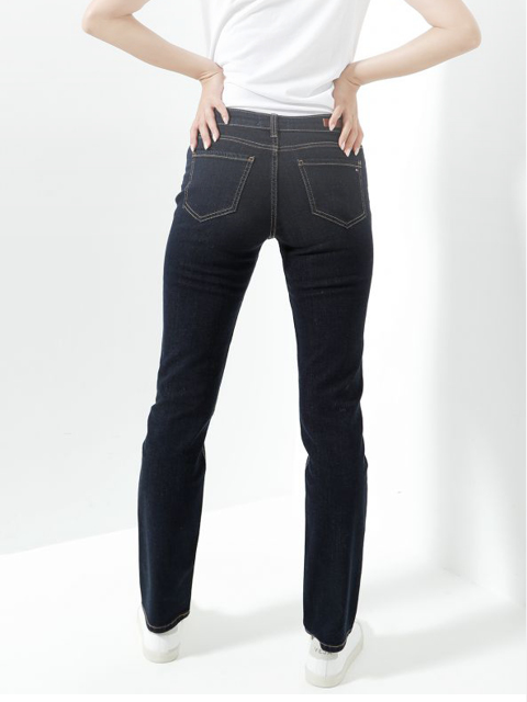 Eine Person, die ein weißes T-Shirt, dunkelblaue Jeans und weiße Turnschuhe trägt, steht mit den Händen in den Taschen vor einem schlichten weißen Hintergrund.