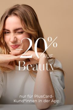Eine Frau mit langen Haaren zwinkert und stützt ihr Kinn auf ihre Hände. Auf dem Bild steht vor beigem Hintergrund „-20% auf Beauty“ und „nur für PlusCard-Kund*innen“.