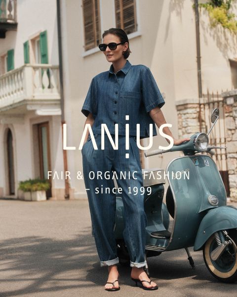 Eine Frau in einem langen, dunkelblauen Kleid sitzt zwischen geschichteten Felsformationen. Der überlagerte Text lautet: "LANIUS FAIR & ORGANIC FASHION - seit 1999.