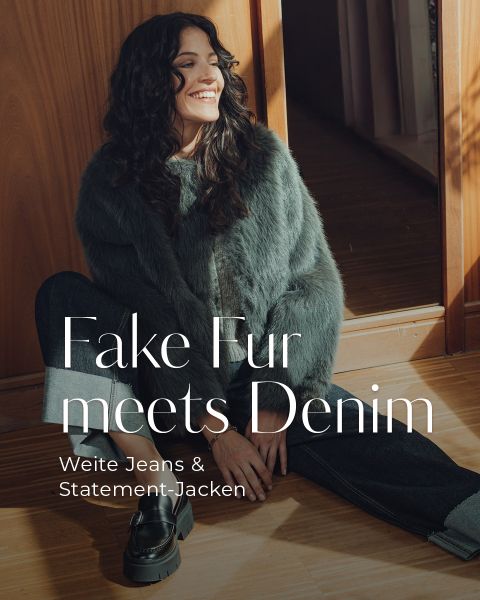 Eine lächelnde Frau mit langen dunklen Haaren sitzt auf einem Holzboden und trägt eine grüne Kunstpelzjacke, dunkle Jeans und schwarze Halbschuhe. Sonnenlicht fällt ein, und ein deutscher Text überlagert das Bild.