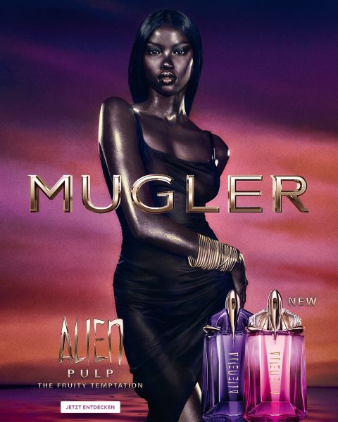 Eine Frau mit strahlend dunkler Haut und glattem schwarzen Haar posiert vor einem violetten Hintergrund. Vor ihr stehen zwei Alien-Parfümflakons von Mugler. Der Text lautet „MUGLER“ und „ALIEN EXTRA INTENSE THE REFILLABLE FRAGRANCES“.