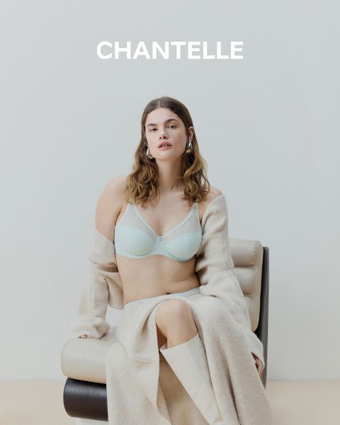 Eine Frau in einem schwarzen, spitzenbesetzten Slip-Kleid und mit Sonnenbrille sitzt auf einem Boot in der Nähe eines Stadtflusses, mit Gebäuden und Bäumen im Hintergrund. Das Wort "CHANTELLE" ist am unteren Rand des Bildes zu lesen.