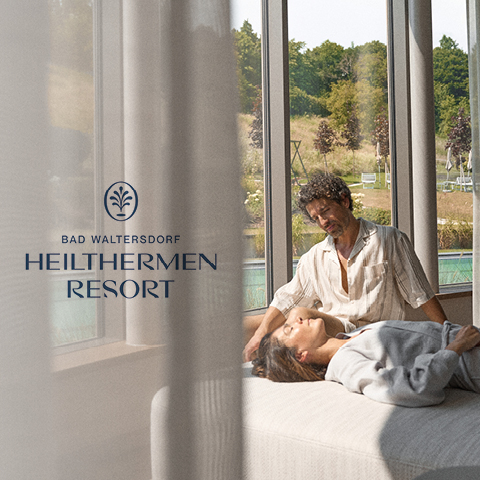 Ein Mann und eine Frau entspannen auf einer Couch in einem sonnendurchfluteten Raum mit deckenhohen Fenstern. Draußen gibt es viel Grün und einen Pool. Der Text auf dem Bild lautet „Bad Waltersdorf Heilthermen Resort“.