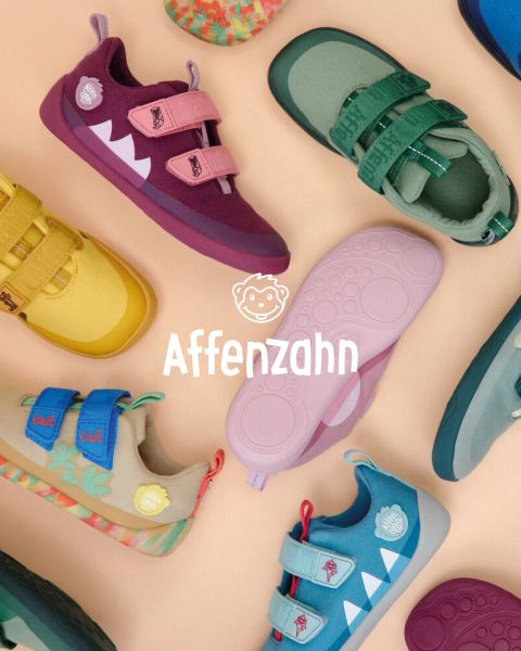 Ein Kind in einem leuchtend orangefarbenen Pullover und gestreiften Hosen sitzt auf einer bunten Fläche und zeigt auf ein Papierflugzeug im Comic-Stil am Himmel. Es lächelt und ist von flauschigen Wolken umgeben. In der Ecke steht „Affenzahn“.