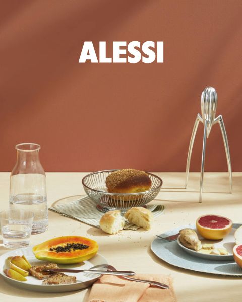 Zwei moderne, geometrische Eierbecher mit Eiern stehen auf einem reflektierenden Tablett, dazu eine Glasschüssel und ein Löffel. Unten in der Bildmitte ist in fetter Schrift „ALESSI“ zu lesen.