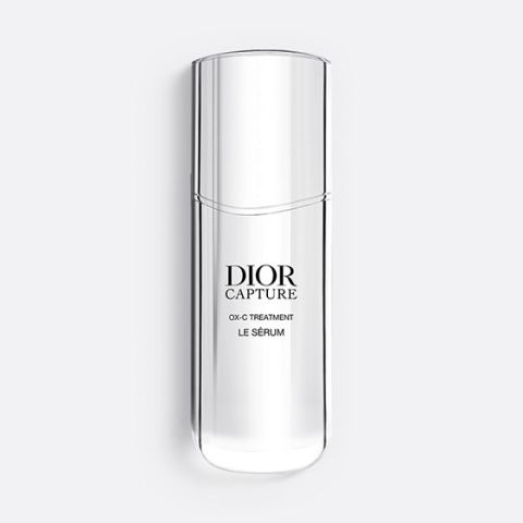 Eine schlanke, durchscheinende Flasche Dior Capture OX-C Treatment Le Sérum. Die Flasche ist hoch und geschwungen, hat ein minimalistisches Design und einen schwarzen Text auf der Vorderseite. Auf einem hellgrauen Hintergrund.