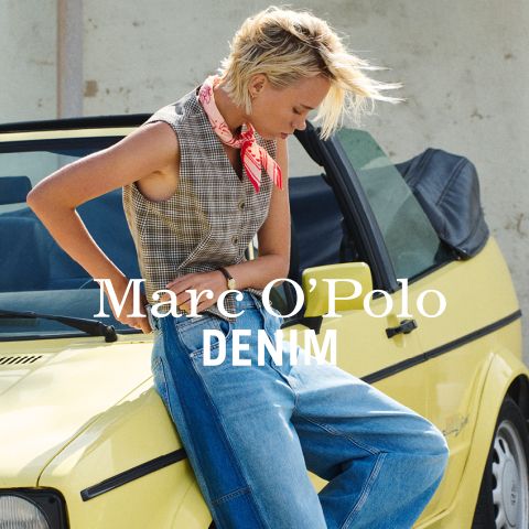 Ein Mann in Jeansjacke und Jeans sitzt an einem Geländer am Meer und hält eine gelbe Blume. Der Text lautet "Marc O'Polo DENIM.