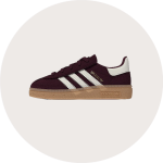 Rosa Wildleder-Sneaker mit weißen Streifen, brauner Gummisohle und goldenem "SAMBA"-Schriftzug an der Seite auf einem hellen, runden Hintergrund.