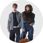 Ein Mann in Jeansjacke und Jeans steht neben einer Frau, die einen Poncho aus Kunstfell und Jeans trägt und eine braune Handtasche in der Hand hält.