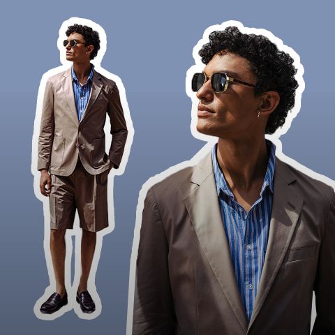 Mann mit Sonnenbrille, der einen hellbraunen Blazer, ein blau gestreiftes Hemd und hellbraune Shorts trägt und selbstbewusst vor einem Hintergrund mit braunem Farbverlauf steht.