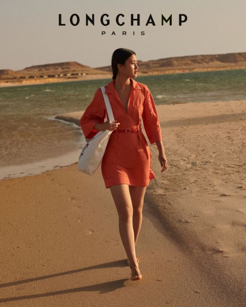 Zwei Frauen stehen dicht beieinander vor einem rosa Hintergrund und präsentieren eine Kollektion von Longchamp Paris. Eine trägt eine gemusterte Jacke, die andere ein einfarbiges Oberteil, beide sind natürlich geschminkt und haben leicht geöffnete Lippen. Darunter wird der Text von Longchamp Paris angezeigt.