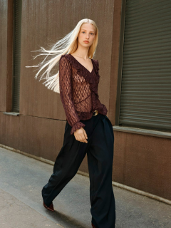 Frau, die auf einer Steintreppe im Freien sitzt und eine langärmelige Jeansbluse mit Rüschendetails und eine passende Jeans mit hoher Taille trägt. Sie hat dunkles Haar, eine Sonnenbrille auf dem Kopf und blickt nachdenklich in die Ferne.