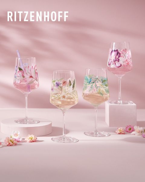 Ein Set farbenfroher, kunstvoller Ritzenhoff-Gläser, gefüllt mit Getränken. Jedes Glas hat ein einzigartiges Design mit lebendigen Mustern und Figuren. Der Hintergrund zeigt Lichtreflexe und weitere Gläser, was eine festliche Atmosphäre schafft.