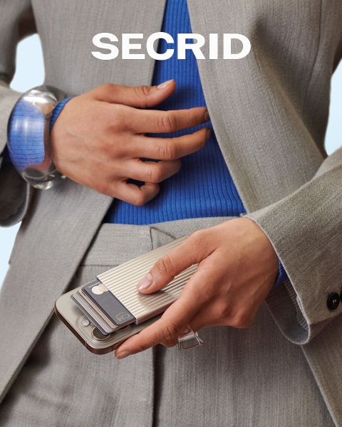 Eine Frau in einem olivgrünen Kleid hält eine passende Secrid-Brieftasche. Der Text lautet: "DESIGNED TO LAST" und das Secrid-Logo ist zu sehen.