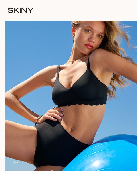 Eine Frau mit geflochtenem Haar schließt einen hellrosa BH mit einem vorderen Verschluss vor einem dunkelroten Hintergrund. Das Wort "SKINY" wird am unteren Rand des Bildes angezeigt.