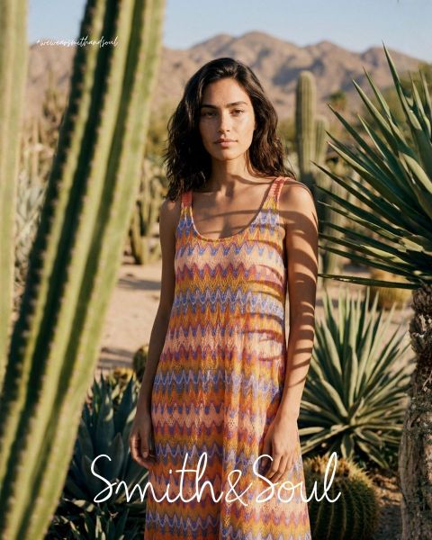 Eine Frau in einem rosa Hemd und einer Strickjacke mit weißer Hose posiert vor einem weißen Hintergrund. Der Text lautet "Smith & Soul" am unteren Rand.