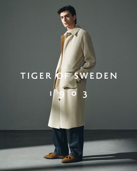 Zwei Männer in eleganten Mänteln stehen im Freien am Wasser unter einem klaren Himmel. Der Text "TIGER OF SWEDEN 1903" steht mittig auf dem Bild.