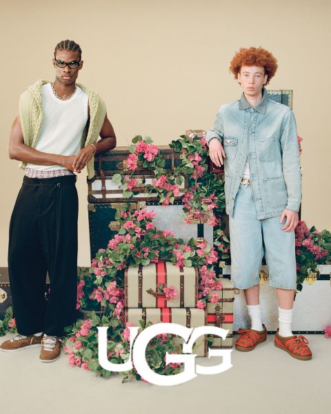 Ein Paar brauner UGG-Wildlederstiefel mit Plüsch-Innenfutter, das auf einer grauen Oberfläche ruht. Das UGG-Logo ist am unteren Rand des Bildes gut sichtbar angebracht.