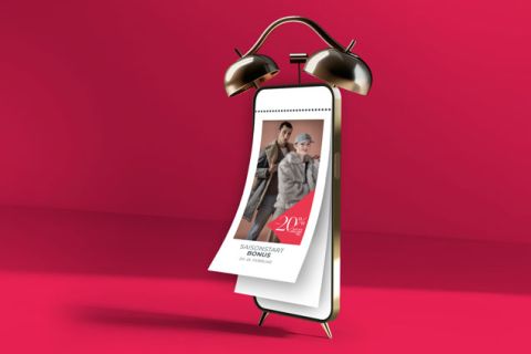 Ein Wecker aus Messing mit Kalenderblättern steht vor einem leuchtend roten Hintergrund. Der Kalender zeigt zwei Personen in Mänteln mit dem Text „20 % Bonus“ in großer Schrift, darunter ein kleinerer Text.