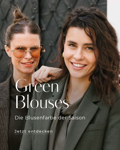 Zwei lächelnde Frauen in grünen Blusen und Blazern stehen zusammen im Freien. Eine trägt eine Sonnenbrille, die andere hat gewelltes Haar. Der deutsche Text auf dem Bild bewirbt grüne Blusen als den Trend der Saison.